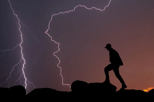 Silhouette of a man walking on top of a mountain, with lightning strikes across the sky