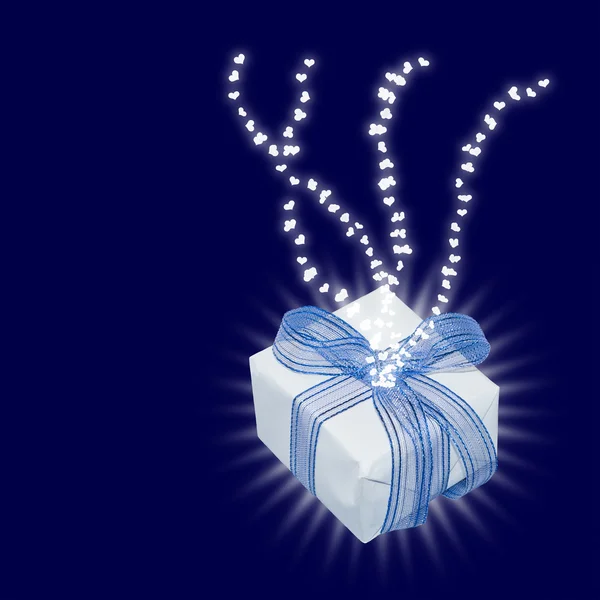 Magic gift with light rays and heart trails, on dark blue background with copy space