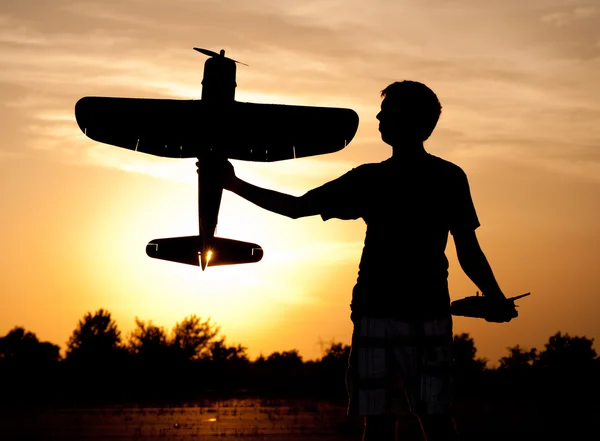 Silhouette of a young man with a model rc airplane against sunset and clouds, with a sunburst