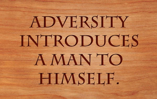Adversity introduces a man to himself - quote by unknown author on wooden red oak background