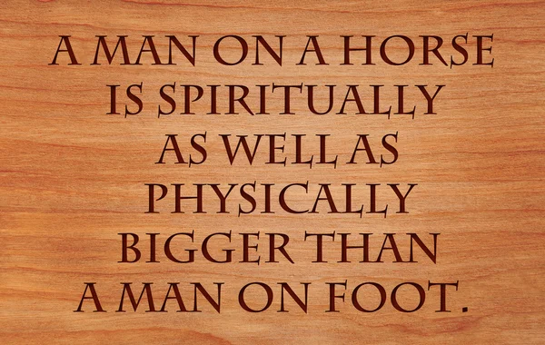A man on a horse is spiritually as well as physically bigger than a man on foot - quote on wooden red oak background