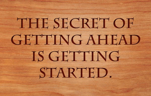 The secret of getting ahead is getting started - motivational quote on wooden red oak background