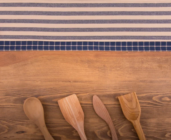 Blue and off white kitchen towels on dark wood background with wooden kitchen utensils