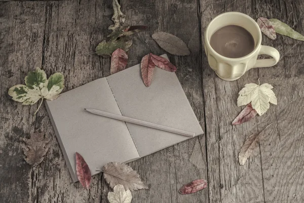 Coffee and notebook on table decorated with dried autumn leaves