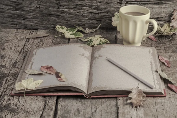 Coffee and notebook on table decorated with dried autumn leaves