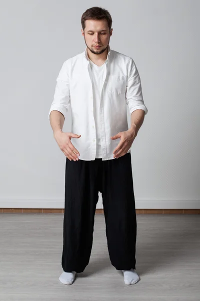 Young man in white shirt and black pants performing tai chi exercise