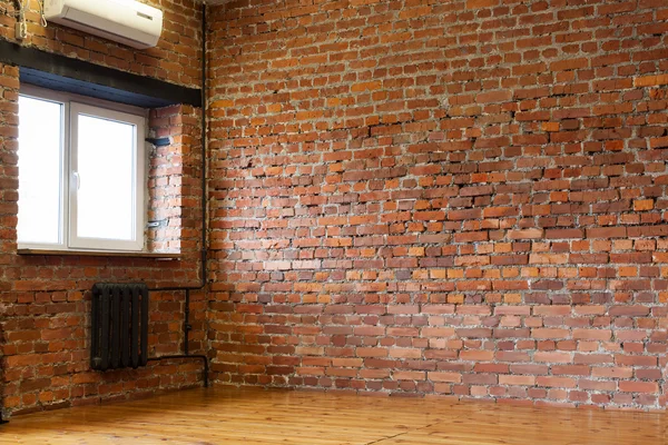 Room with a window, red brick walls and wooden flooring of boar