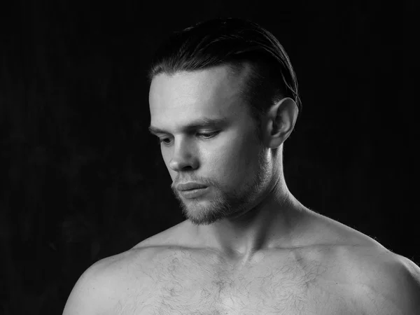 Black and white close-up portrait of a naked strong guy on a gra