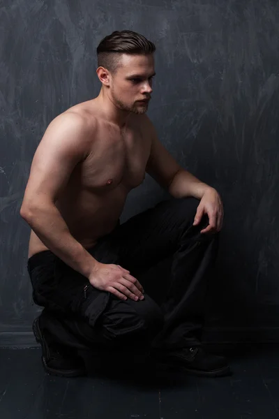 Fitness model with naked torso in black pants and boots sitting