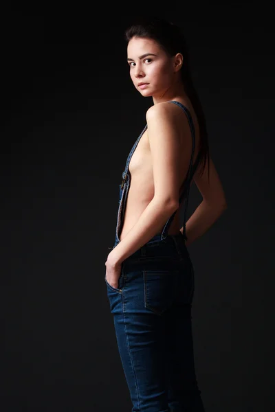 Young  brunette woman in jeans overalls with naked torso