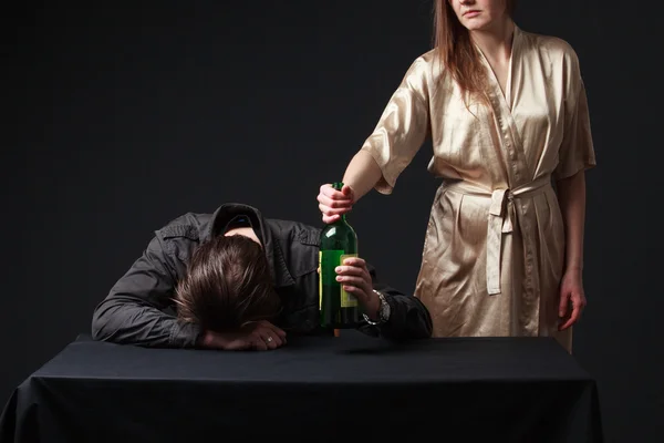 Alcoholism. Drunk man is sleeping on the table with the bottle i