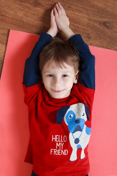Little boy in a red shirt is laying on  a mat , doing exercise