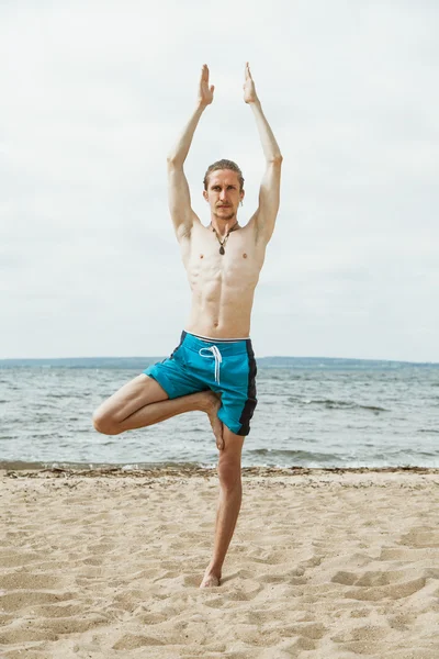 Thin man doing yoga on the beach