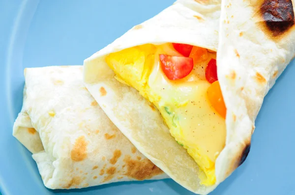 Scrambled egg breakfast burrito with tomatoes and green onion an