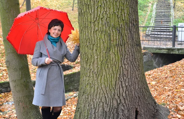 The woman of average years costs under a red umbrella in autumn