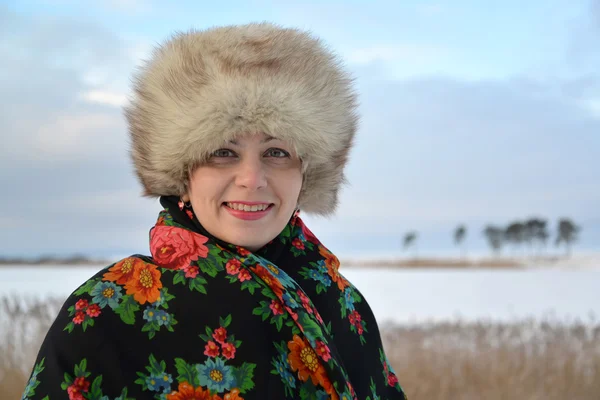 Portrait of the woman of average years in a fur cap and a colorful shawl against the winter lake