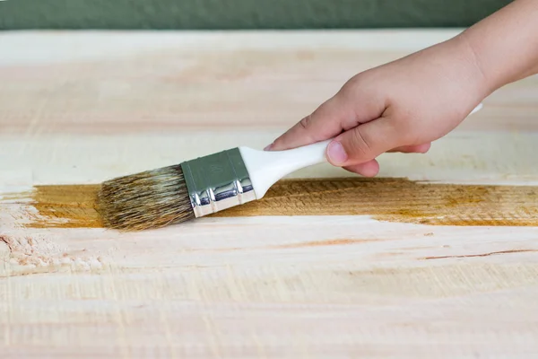 Varnishing a wooden shelf using paintbrush, kid hand