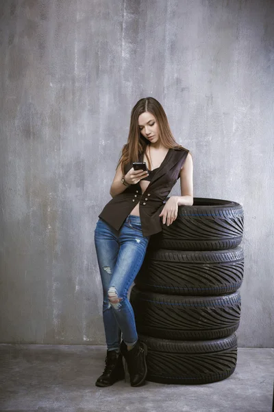 Young girl with a mobile phone, is leaning against the tires on