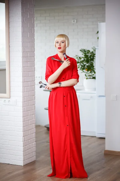 Emotional woman in a red dress with makeup brushes in their hand