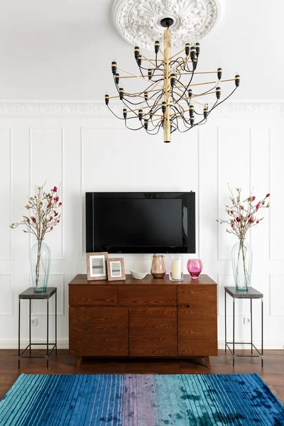 Interior of a room with white walls, a TV and a dresser in a con