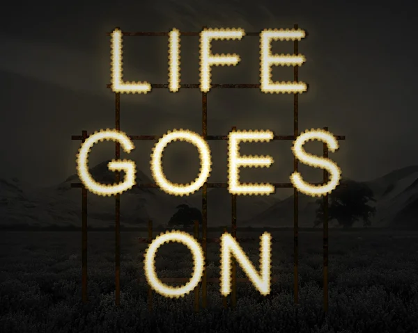 Life Goes On inspiring text in lights against dark landscape bac