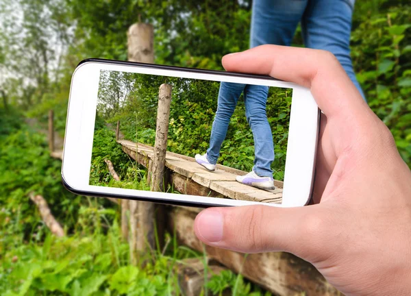 Hands taking photo tourist walking on a wooden bridge with smartphone.