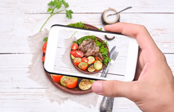 Hands taking photo grilled rib with grilled vegetables with smartphone.