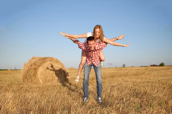 Young man and woman having fun in a harvested field near a bale of hay.