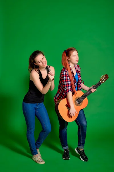 Two young women have fun, sing and play classical guitar