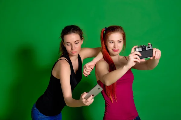 Two young women doing selfie with an old camera and a smartphone