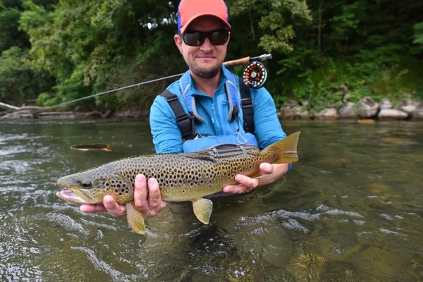 Fly-fisherman holding brown trout