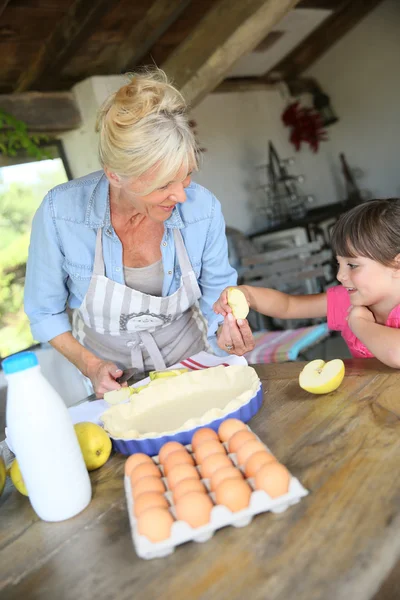 Grandmother cooking pie with little girl