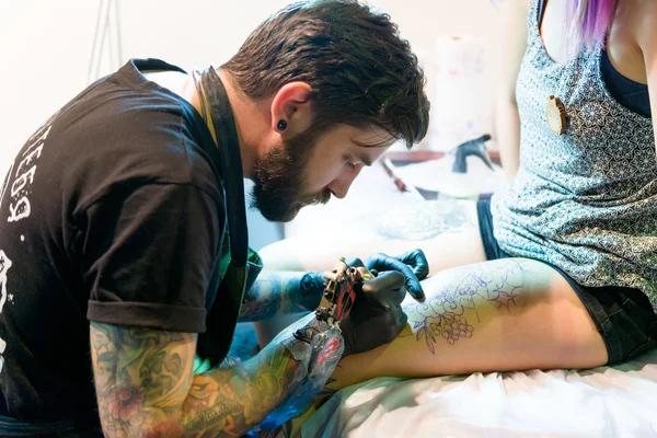 MINSK, BELARUS - SEPTEMBER 19, 2015: Professional tattoo artist doing tattoo on woman leg.