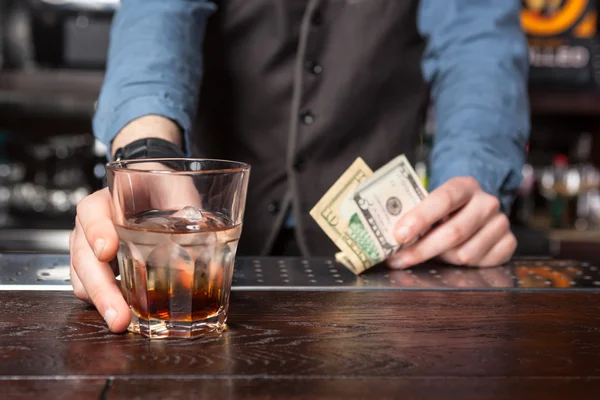 Barman with whiskey glass and money in his hands.