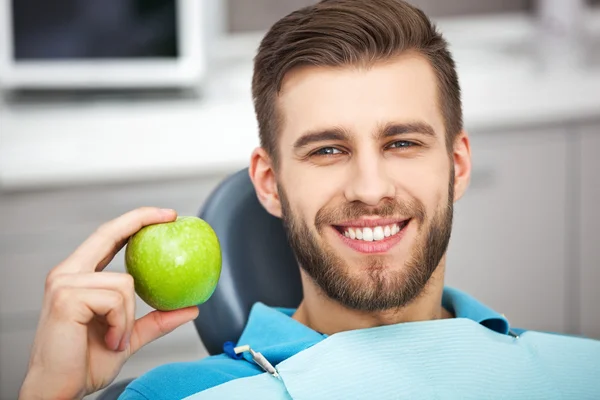 Portrait of happy patient in dental chair with green apple.