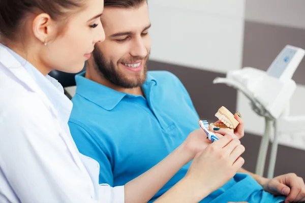 Dentist explaining to male patient how to brush his teeth.