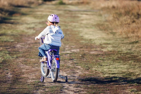 Small funny kid riding bike with training wheels.