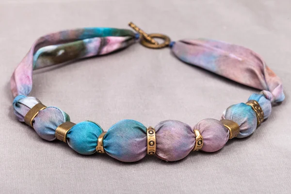 Necklace from painted silk and brass beads on gray