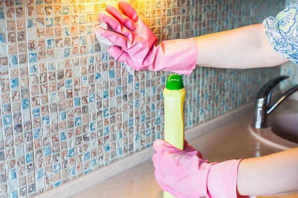 Woman washes kitchen wall with detergent