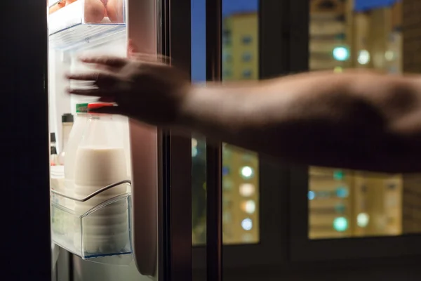 Hand reaches for milk bottle in fridge in night