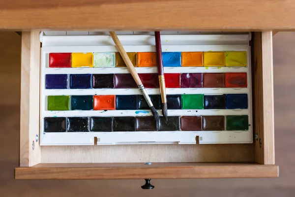 Watercolor paints set and brushes in open drawer