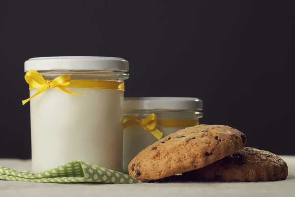Two jars of milk and cookies with yellow ribbon on a dark backgr