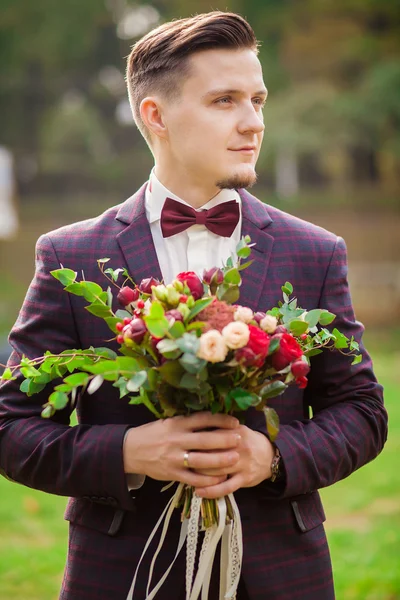 The groom holds a bouquet and smiles. Portrait of the groom in t
