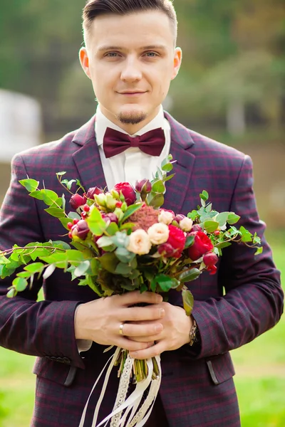 The groom holds a bouquet and smiles. Portrait of the groom in t
