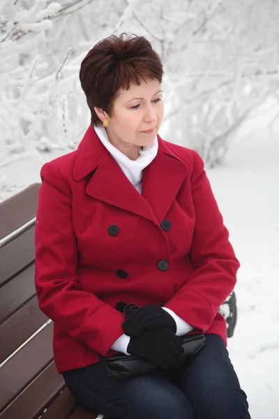 Attractive elderly woman sitting on bench on winter snowy street