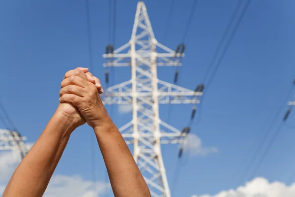 Hands crossed in assent and power transmission lines against blu