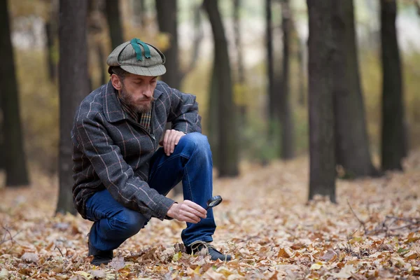 Man detective with a beard exploring footprint on the autumn lea