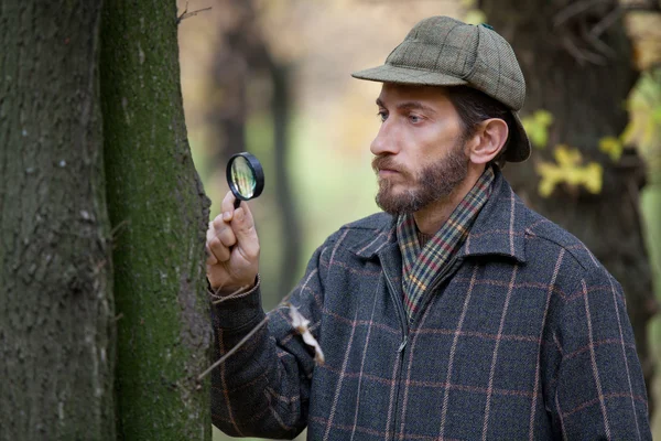 Man detective with a beard studying tree trunk in autumn forest