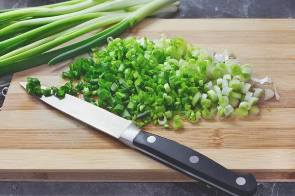 Handful of chopped green onions on striped wooden board
