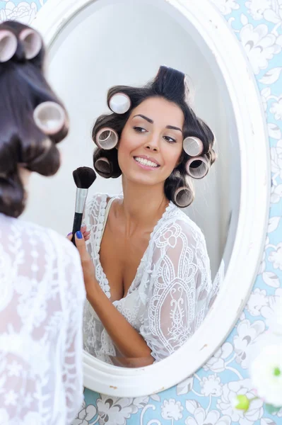 Beautiful woman in hair curlers puts on morning makeup